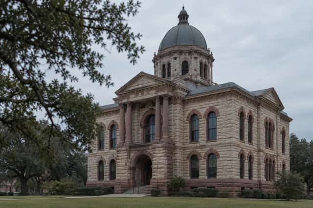 The limestone facade and clock-free cornice of a historic Texas county courthouse under a wide overcast sky